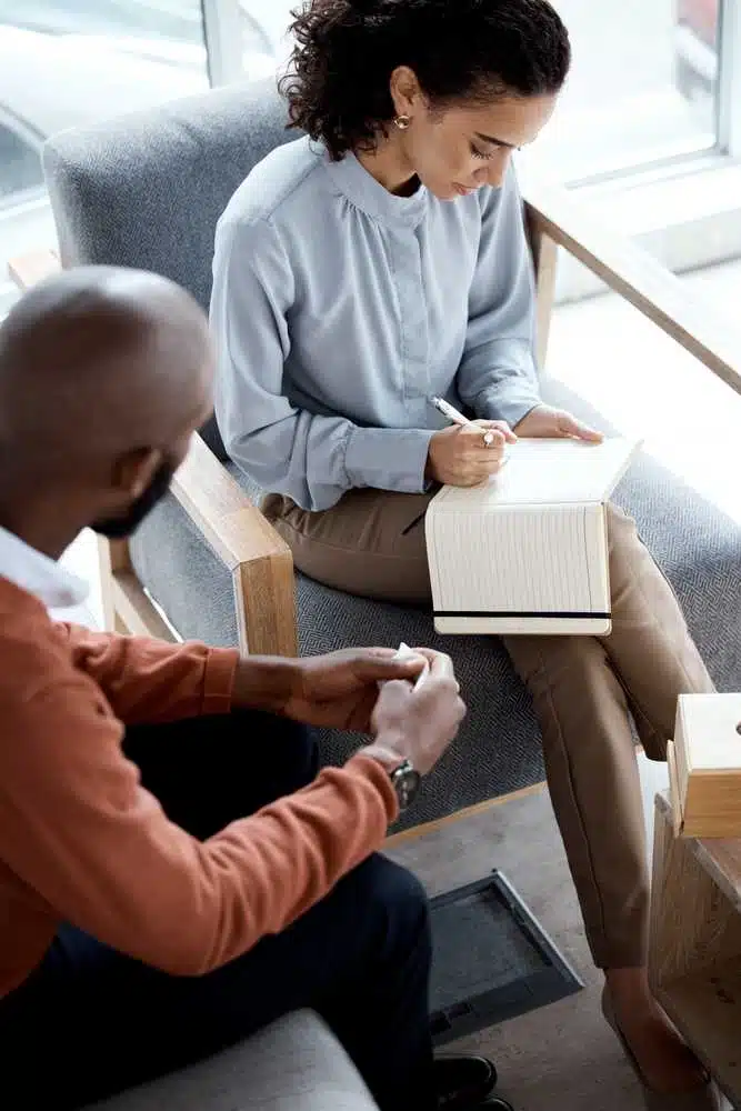 A woman writes in notebook while a man sits next to her.